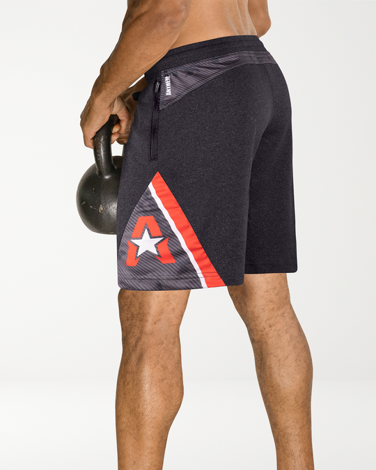 Man wearing Anthem Athletics Isoflex 9" training shorts in Volcanic Black Camo holding a kettlebell on a white background